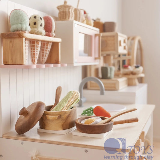 Wooden toy kitchen set with handcrafted mahogany pan, pot with lid, and utensils displayed on a play kitchen counter.