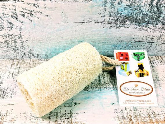 Natural 4-inch loofah sponge with rope handle resting on a rustic blue wooden surface.